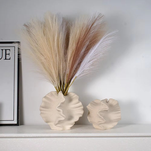 Beige ceramic coral vase with wavy, organic texture on white tabletop, filled with neutral pampas grass