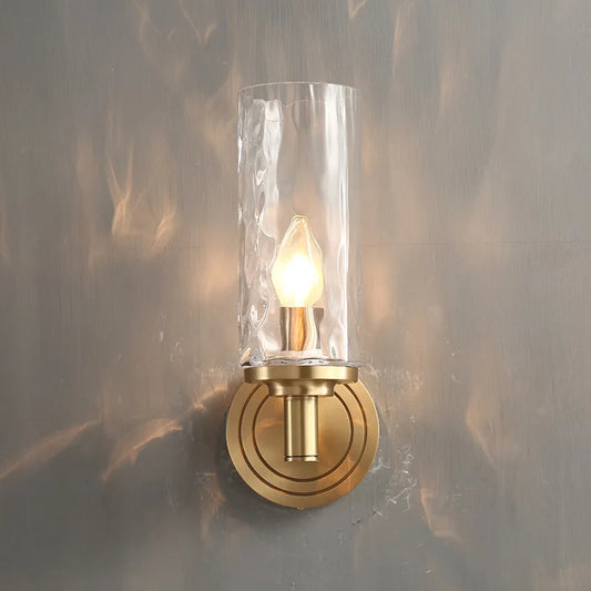 A modern wall-mounted sconce with a clear glass shade and a gold-colored base, featuring an LED light source.