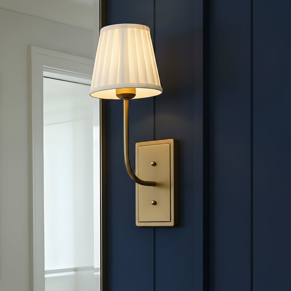 Wall-mounted lamp with a white shade and gold fixture on a light gray wall.