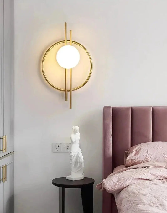Two black, modern design wall sconces with a golden glow, mounted on a wall on either side of a bed with a framed picture and a small plant beside it.