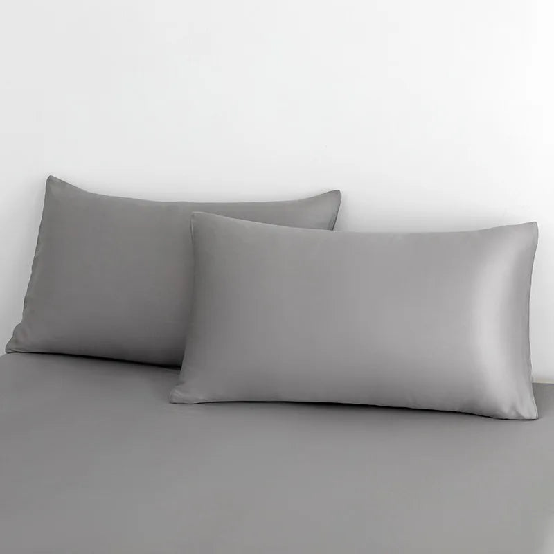 A luxurious bed adorned with a sleek grey sheet and plush pillows, showcasing the elegance of the EleganceSatin Summer Bedding Set.
