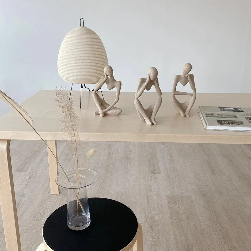 A table adorned with "The Thinker Statue Tabletop Art", featuring a seated woman statue lost in deep thought.