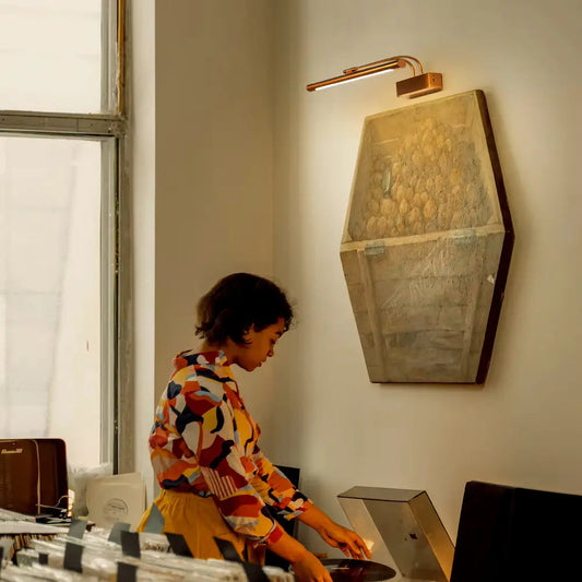 Slim brass LED wall lamp casting warm light over artwork in living room setting