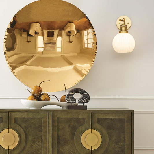 Round gold mirror above a wooden cabinet with decorative items.