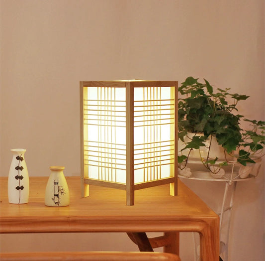 Wooden table with a lamp, vases, and a plant against a beige wall