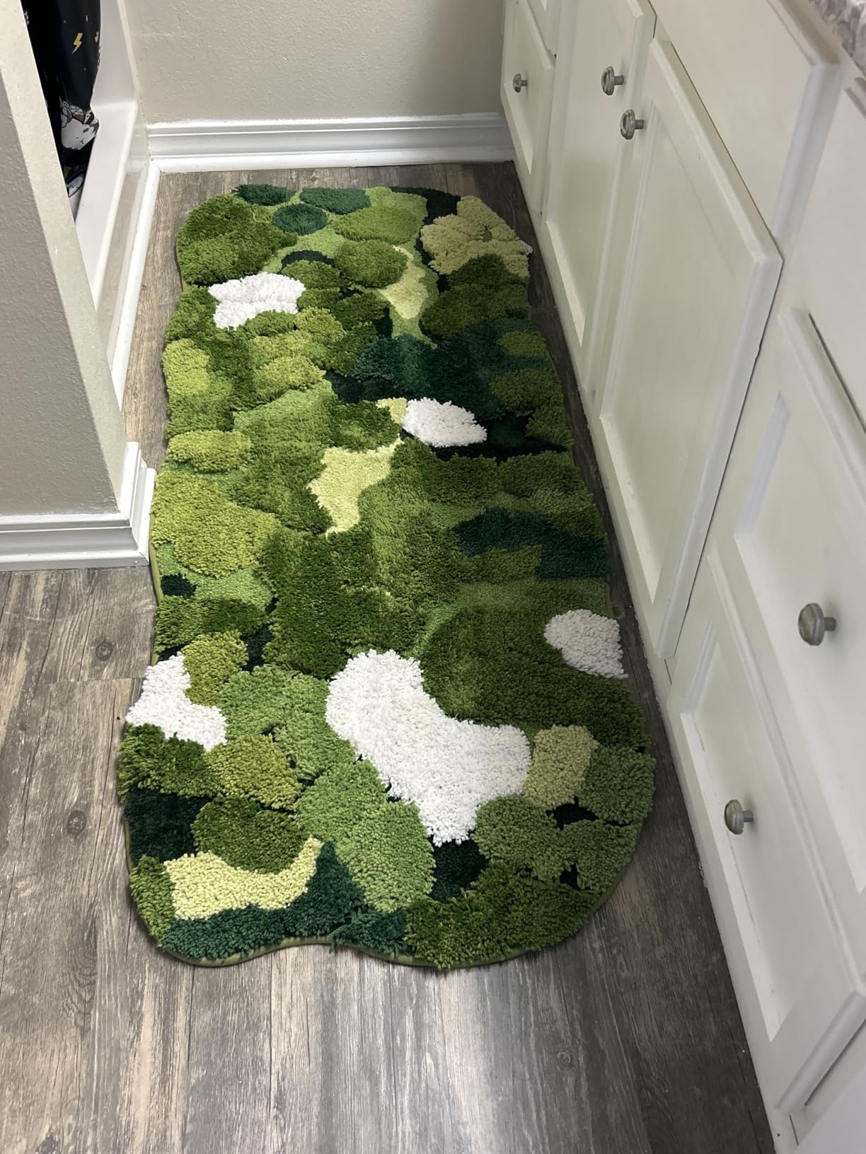 Green camouflage-patterned rug on a wooden floor next to white cabinets.
