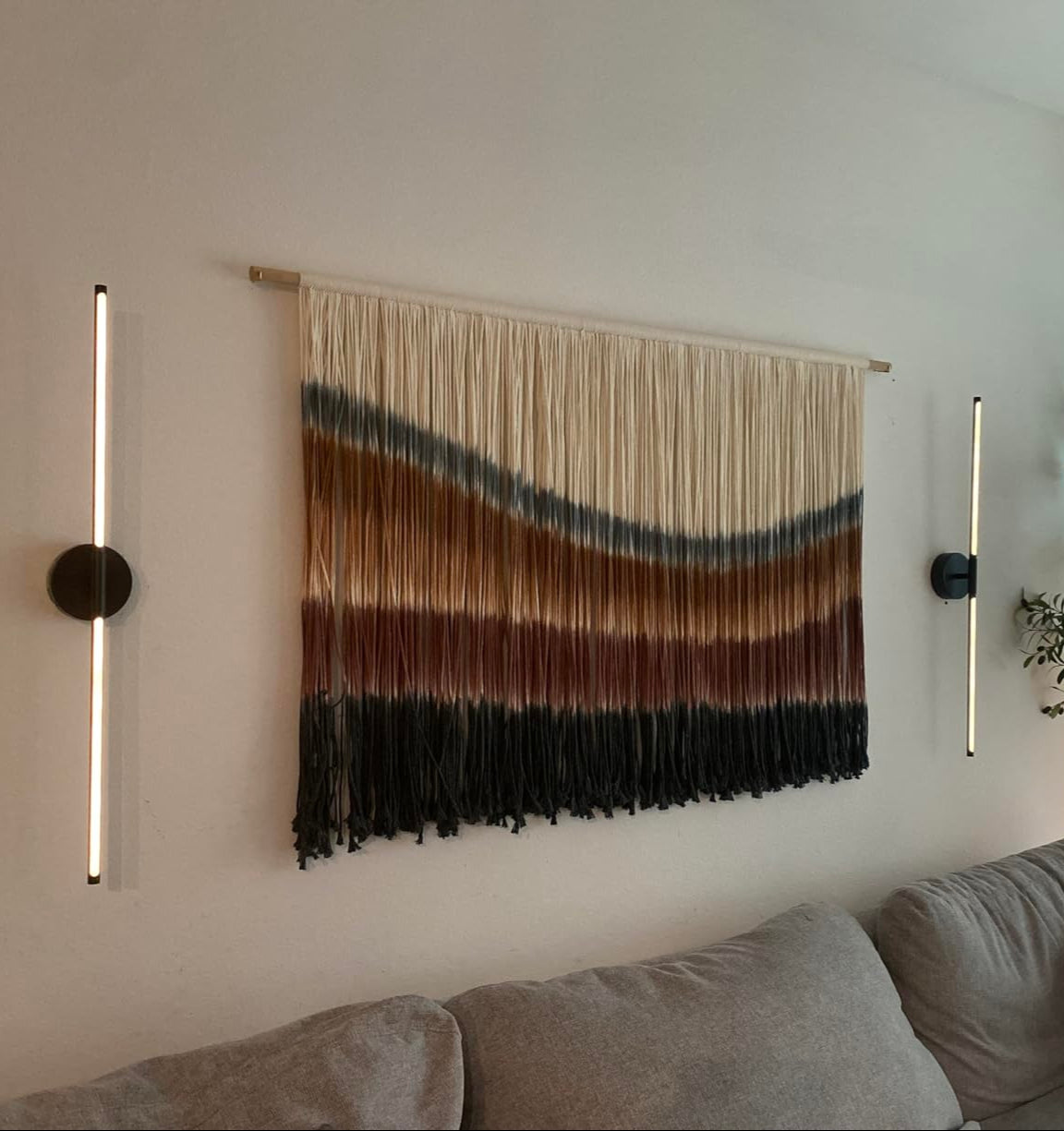 Woven wall art piece with gradient colors above a sofa in a living room.