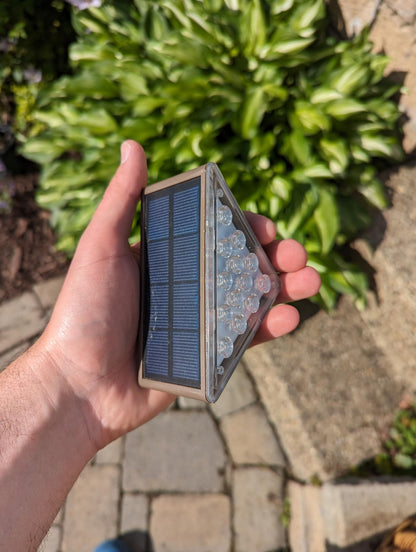 Hand holding a small solar panel device with greenery in the background