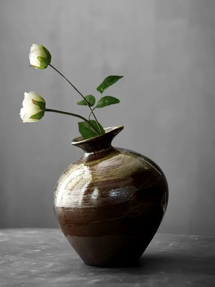 A brown ceramic vase with a rustic texture, containing a bunch of white flowers.