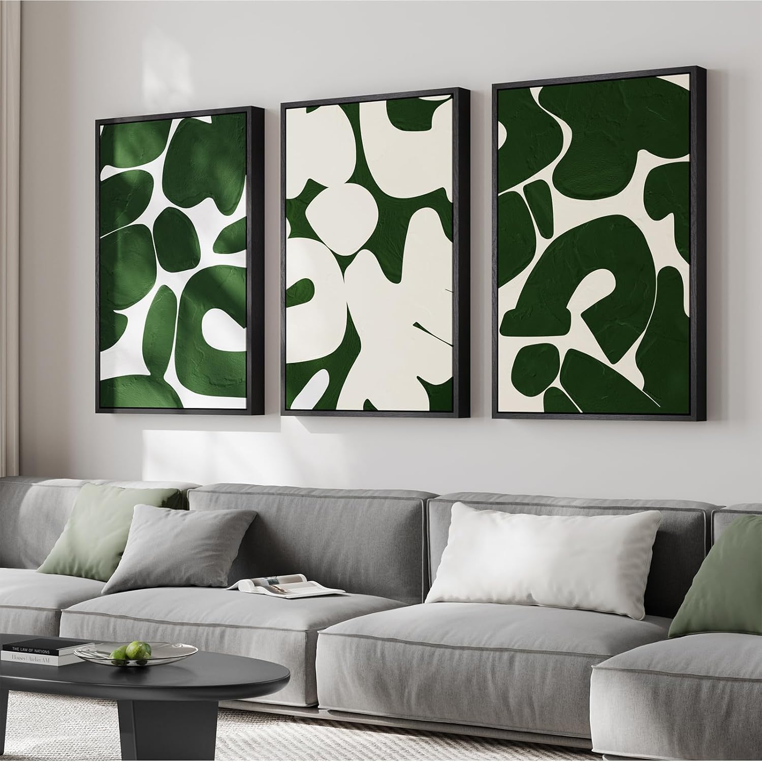 Three abstract art pieces in green and white on a wall above a gray sofa.