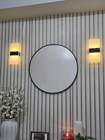 Round mirror on a wall with two wall lights and decorative items below.