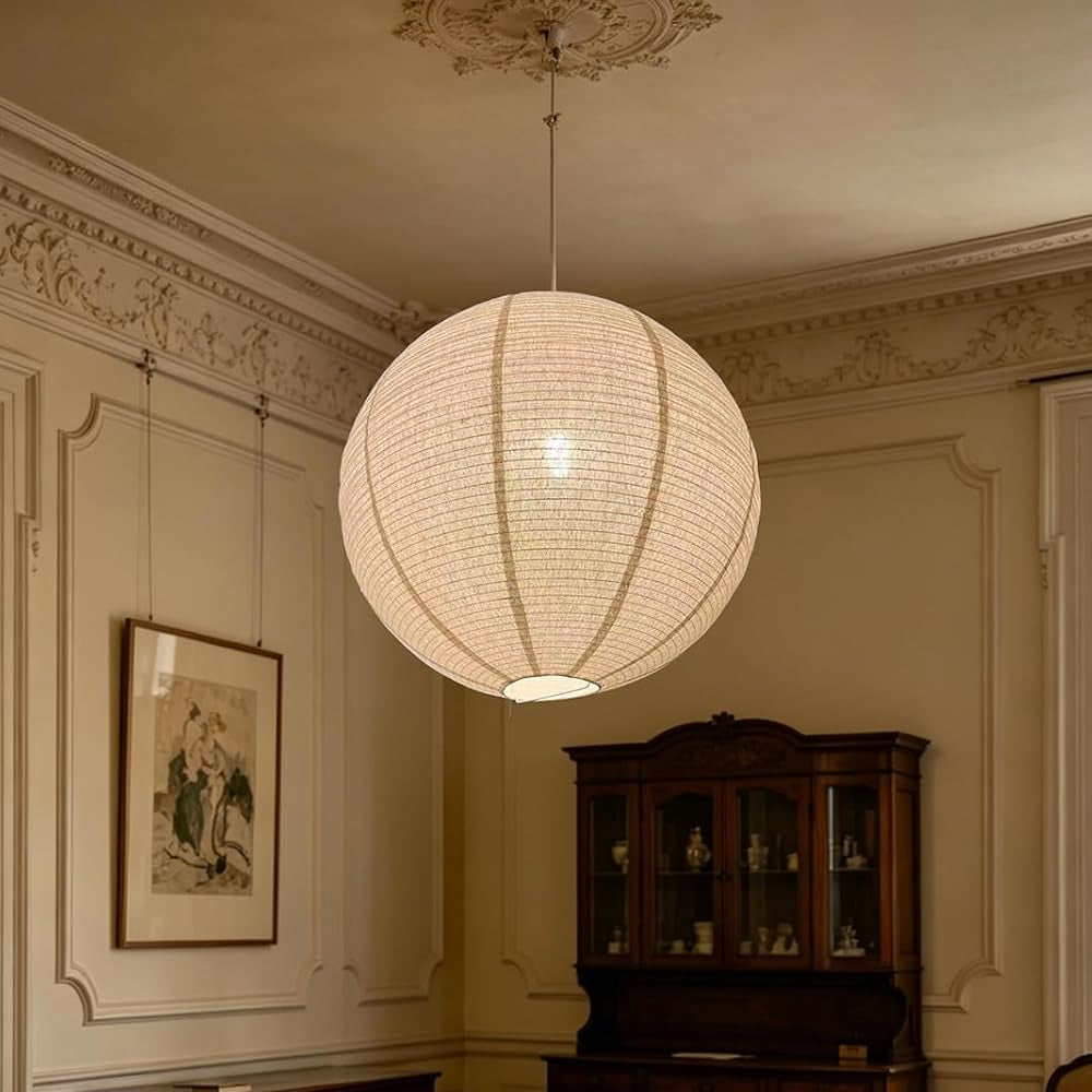 A large spherical white paper lantern pendant light hangs in an elegant vintage room with cream walls, a dark wood hutch, and a patterned rug.