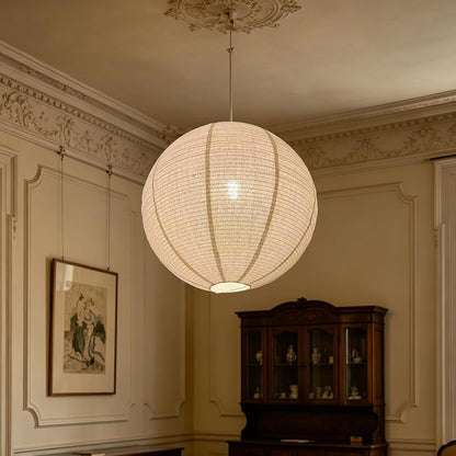 A large spherical white paper lantern pendant light hangs in an elegant vintage room with cream walls, a dark wood hutch, and a patterned rug.