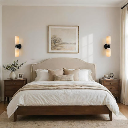 Neatly made bed in a bedroom with wall art and side lamps.
