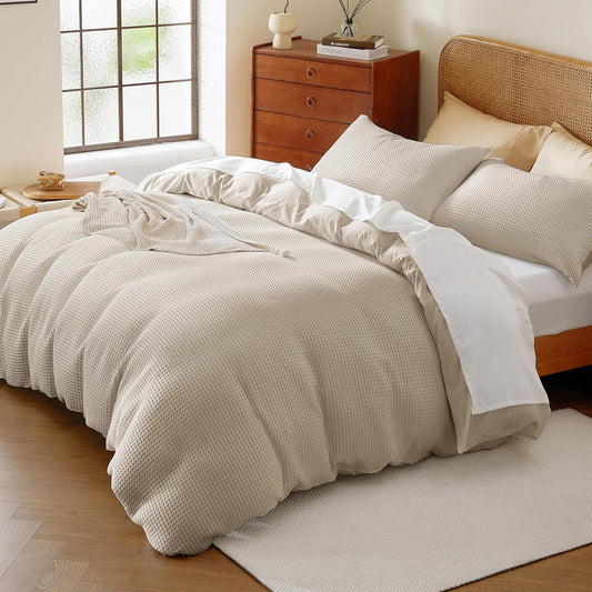 Neatly made bed with beige comforter and pillows in a bedroom setting.