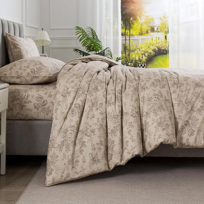 A beige and gray floral patterned comforter set styled on a bed in a bright, modern bedroom with white walls, a window, and a plant.