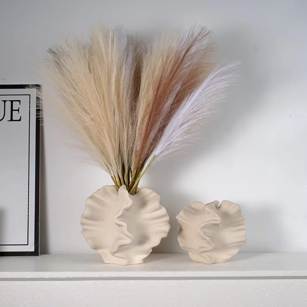Beige ceramic coral vase with wavy, organic texture on white tabletop, filled with neutral pampas grass