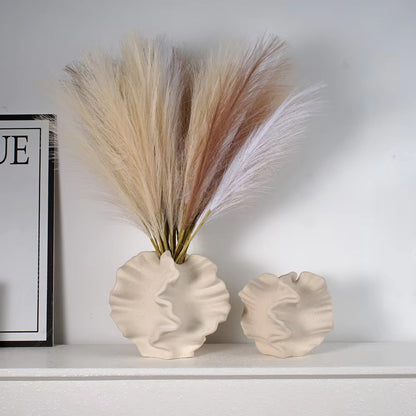 Beige ceramic coral vase with wavy, organic texture on white tabletop, filled with neutral pampas grass