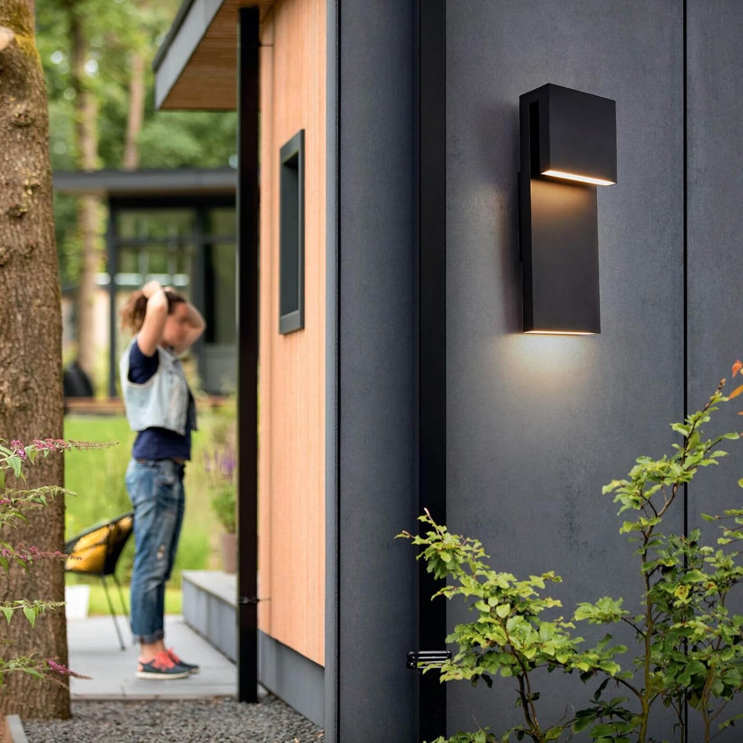 Modern outdoor wall light fixture on a house exterior with a person taking a photo in the background.