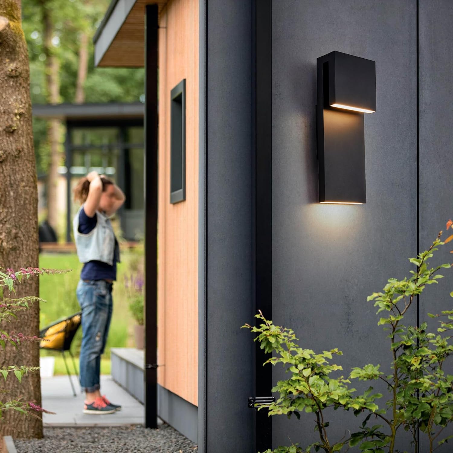 Modern outdoor wall light fixture on a house exterior with a person taking a photo in the background.