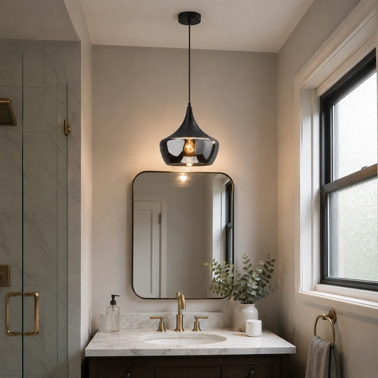 A modern black pendant light with a smoky glass shade hangs over a bathroom vanity with a white marble countertop, gold faucet, and a wall mirror.