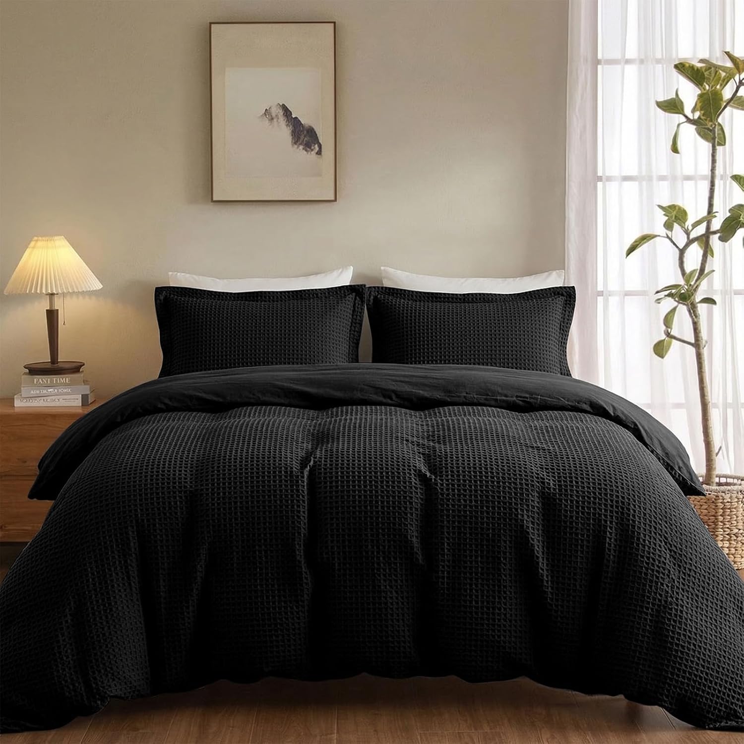 A black textured waffle-weave bedding set, including a duvet cover and two matching pillowcases, styled on a bed in a warm, modern bedroom setting.