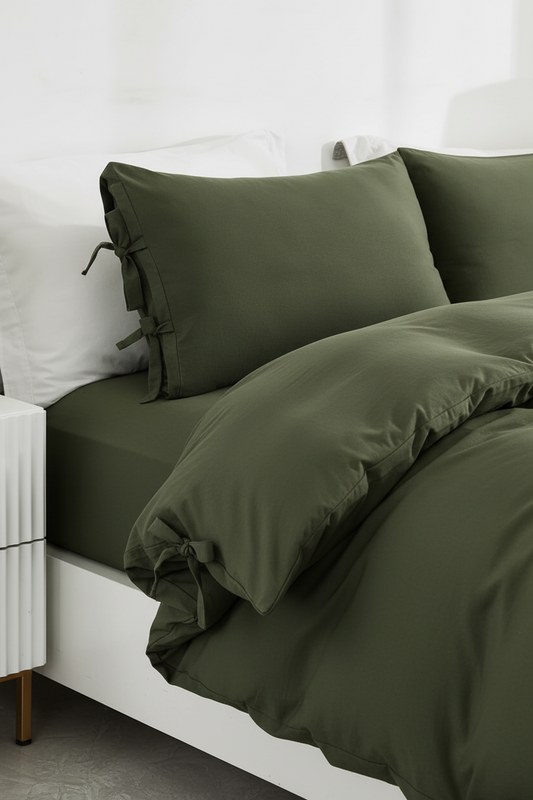 Olive green bedding set on a bed with matching pillowcases, white pillows, and a white headboard in a bright bedroom setting.