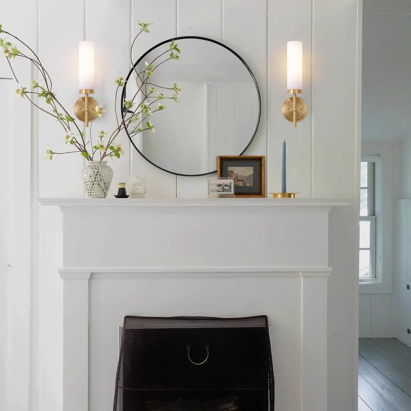 Decorative mantel with a mirror, candles, and a vase on a white wall.