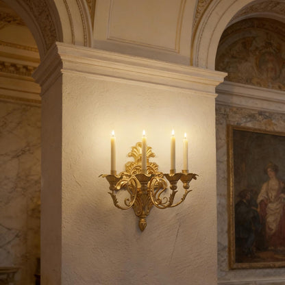 Gold wall sconce with candles on a marble wall in an ornate room.