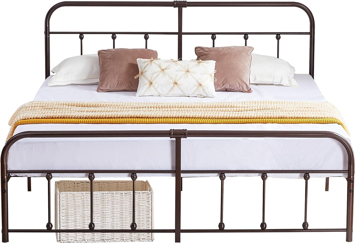 A dark brown metal bed frame with a tall headboard and footboard, styled with white bedding, brown and cream pillows, and a yellow knit throw blanket. A woven storage basket is tucked underneath the footboard.