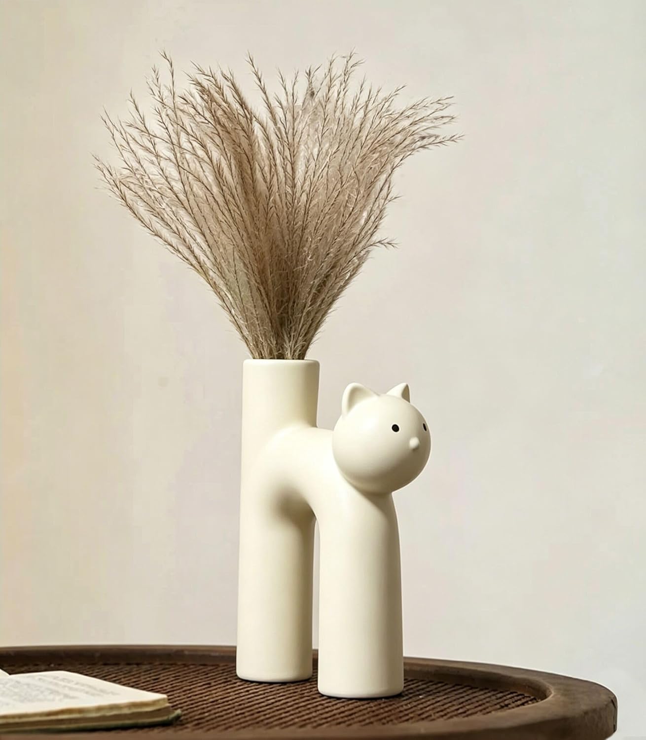 White ceramic vase shaped like a cat with dried plants on a wooden surface