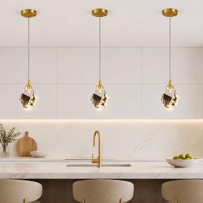 Three modern pendant lights with gold-finished canopies and clear faceted glass shades hang over a white marble kitchen island in a bright, contemporary kitchen.