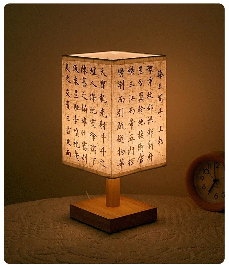 Wooden table lamp with a lampshade featuring Chinese characters, placed on a surface with a clock in the background.