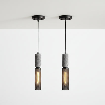 Two matching pendant lights shown side by side on a plain white background. Each light has a black ceiling canopy and cord, a textured gray cylindrical middle section, and a dark mesh lower shade with a glowing warm bulb inside.