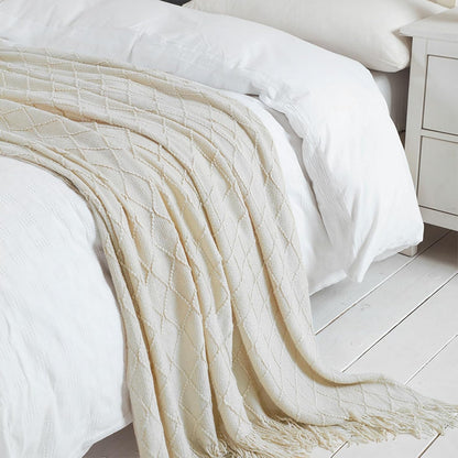 White textured blanket draped over a bed in a softly lit room.