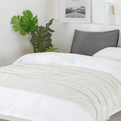 Bed with white bedding and a gray pillow, plant, and framed picture in the background.