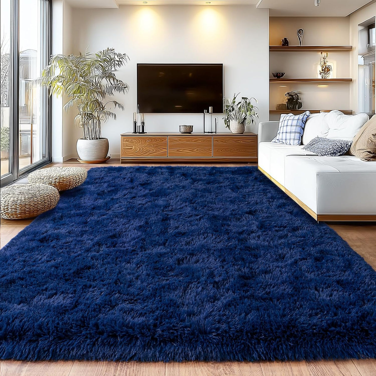 A large, plush navy blue shag area rug styled in a modern living room setting with a white sofa, wooden media console, and potted plants.