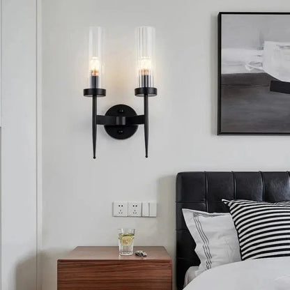 A modern double head gold wall sconce with clear glass lampshades, featuring a gold finish, mounted on a wall.