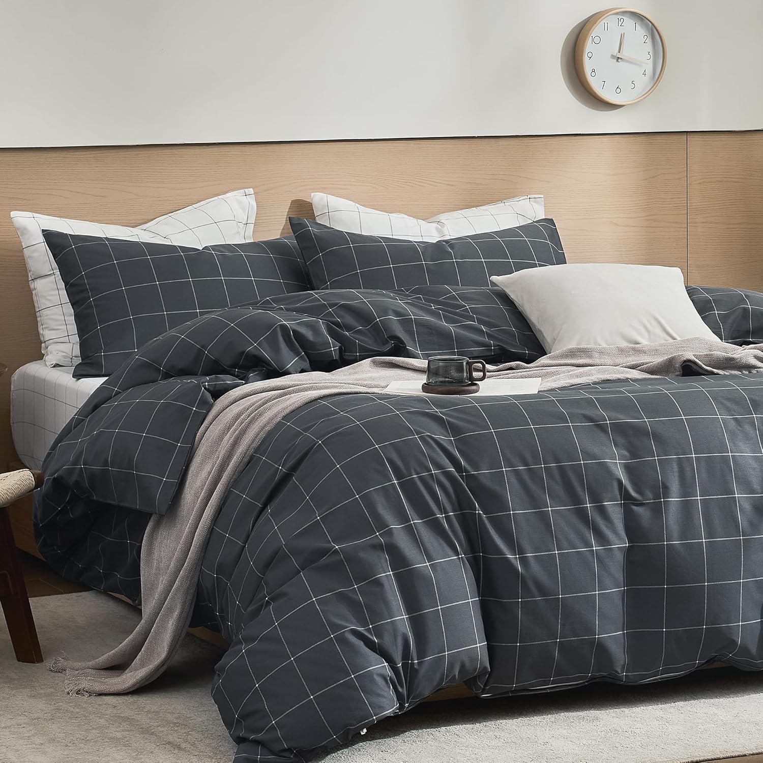 A bed dressed in a dark charcoal gray and white windowpane plaid bedding set, styled with a light beige throw blanket and white accent pillows in a modern bedroom setting.