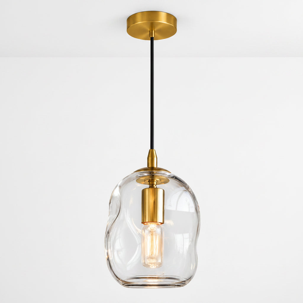 A modern pendant light with a wavy, organic-shaped clear glass shade, a brushed gold ceiling canopy and collar, and a black hanging cord with a gold accent.