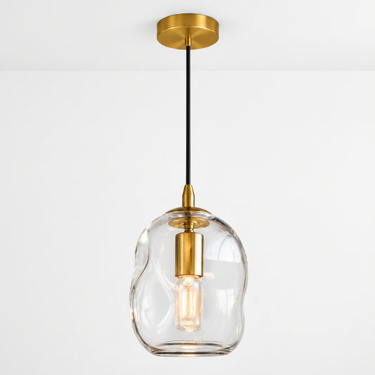 A modern pendant light with a wavy, organic-shaped clear glass shade, a brushed gold ceiling canopy and collar, and a black hanging cord with a gold accent.