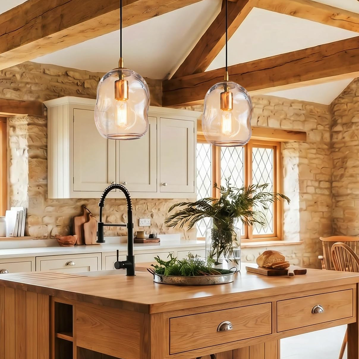 Two modern glass dome pendant lights with warm Edison bulbs hanging over a rustic wooden kitchen island in a stone and wood kitchen.
