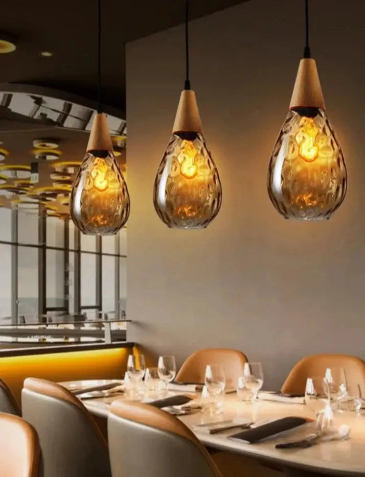 Three modern pendant lights with a glass and stone design hanging over a dining table in a restaurant setting.
