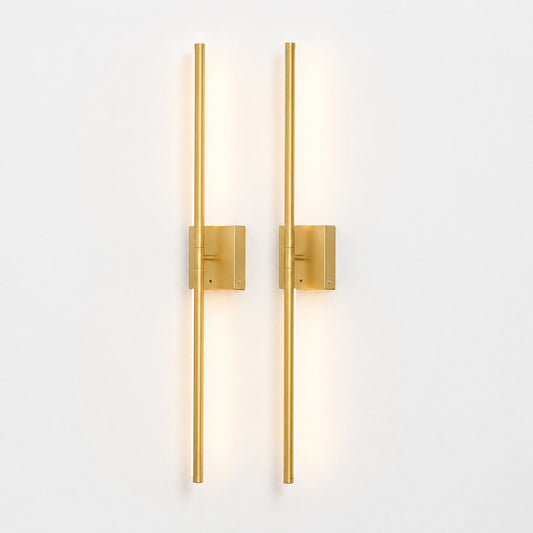 Two modern vertical wall sconces with slim cylindrical rods and square backplates in a brushed gold finish, mounted side by side on a plain white wall and casting a warm light.