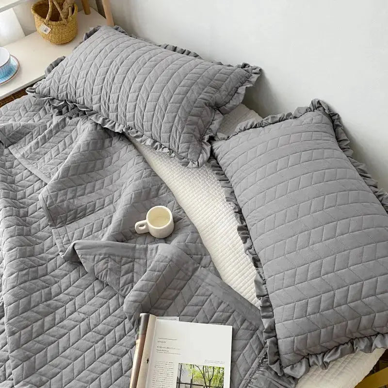Gray quilted bedding set with pillows on a bed.