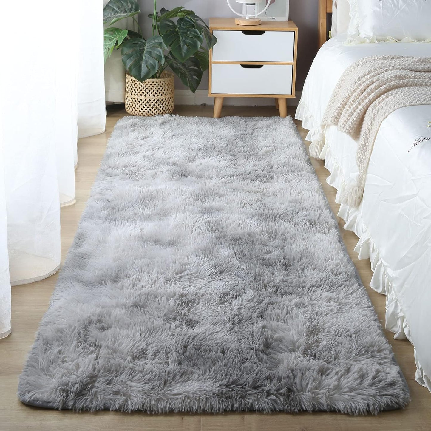 Gray shaggy rug on a wooden floor in a bedroom setting with a bed and nightstand.