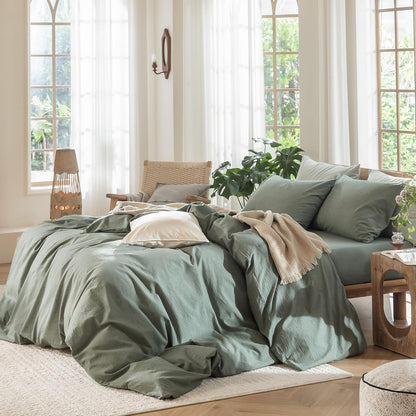Neatly made bed with green bedding in a bright bedroom with large windows.