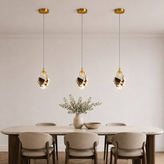 Three modern gold pendant lights with faceted glass globes hang above a dining table with chairs in a bright, minimalist room.