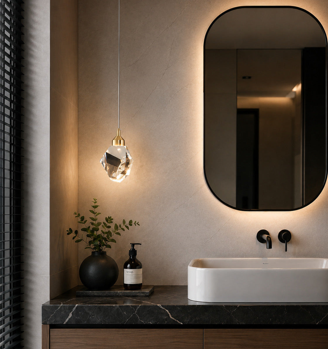 A modern bathroom vanity featuring a white vessel sink, a dark marble countertop, a wall-mounted oval mirror with warm backlighting, and a hanging pendant light with a faceted glass shade.