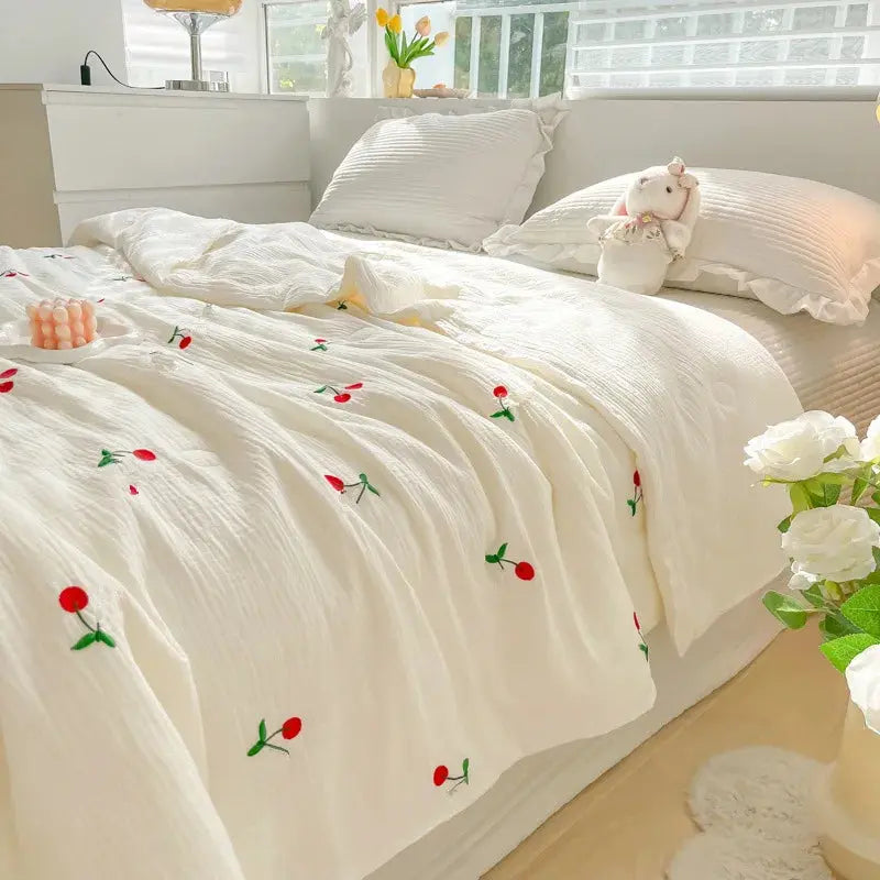 White floral embroidered comforter on a bed with pillows and flowers.